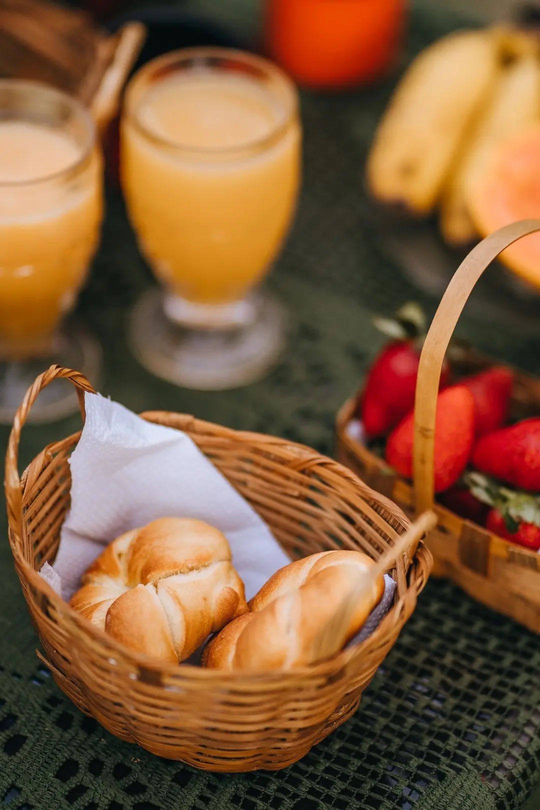 Cesta de pãezinhos com sucos de laranja e morangos, no café da manhã servido no jardim