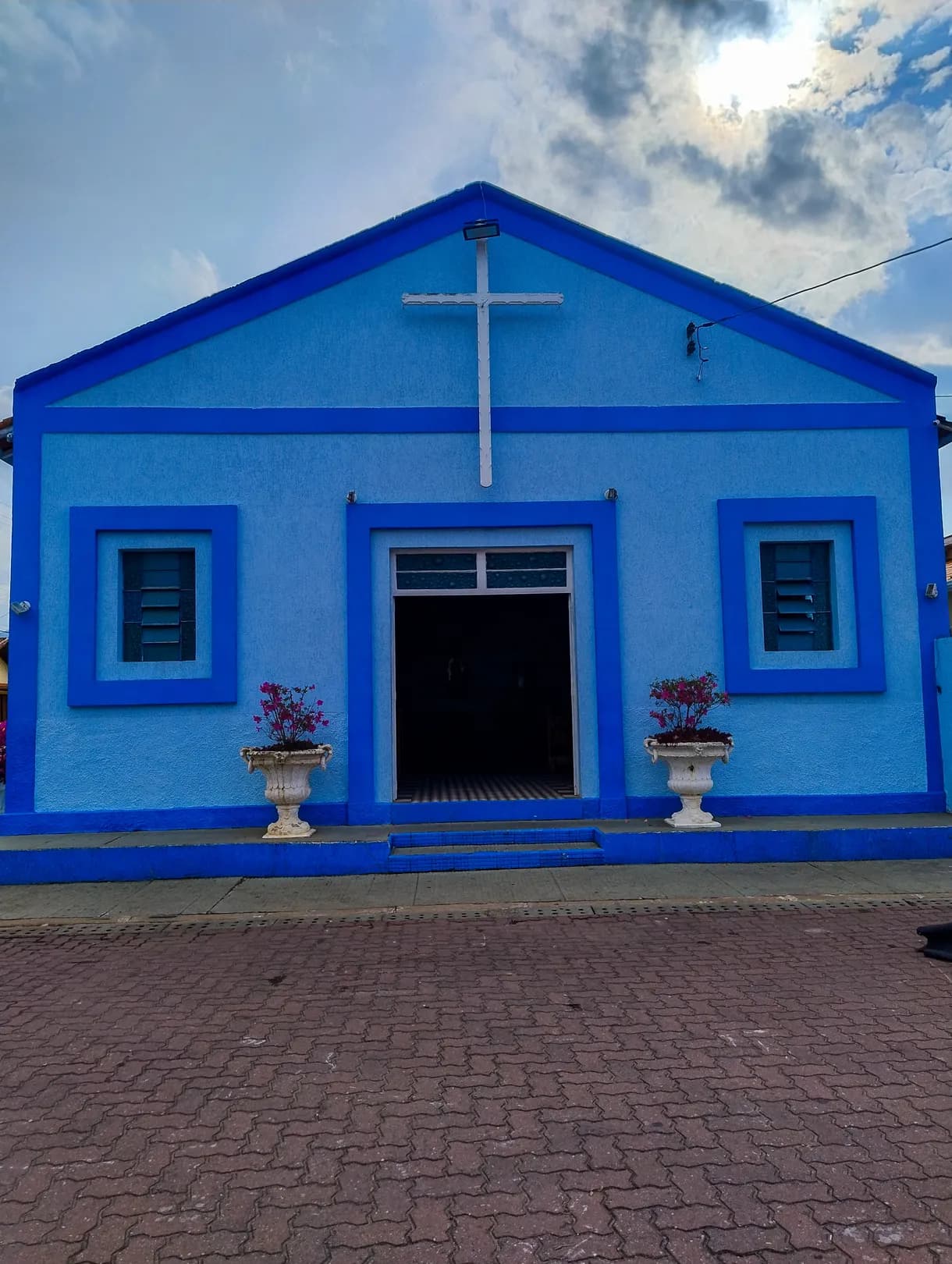 Fachada azul da Igreja Nossa Senhora dos Remédios, com a cruz branca no frontão e vasos de flores na porta