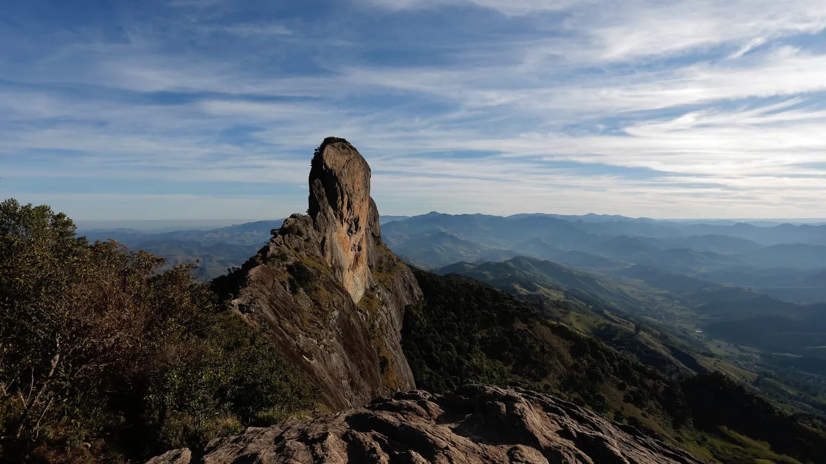 Pedra do Baú vista do alto da trilha, com o monólito recortado contra o céu e o mar de montanhas ao fundo
