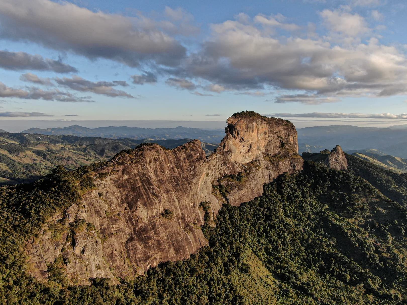 Vista aérea do maciço da Pedra do Baú à luz dourada do fim de tarde, com a serra ao fundo