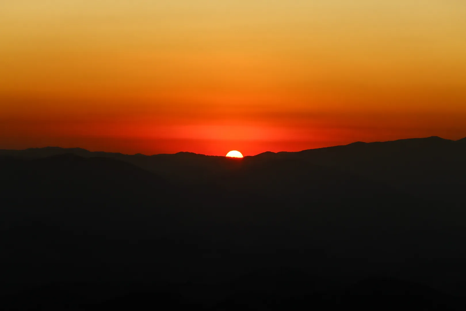 Pôr do sol alaranjado sobre as silhuetas das serras da Mantiqueira
