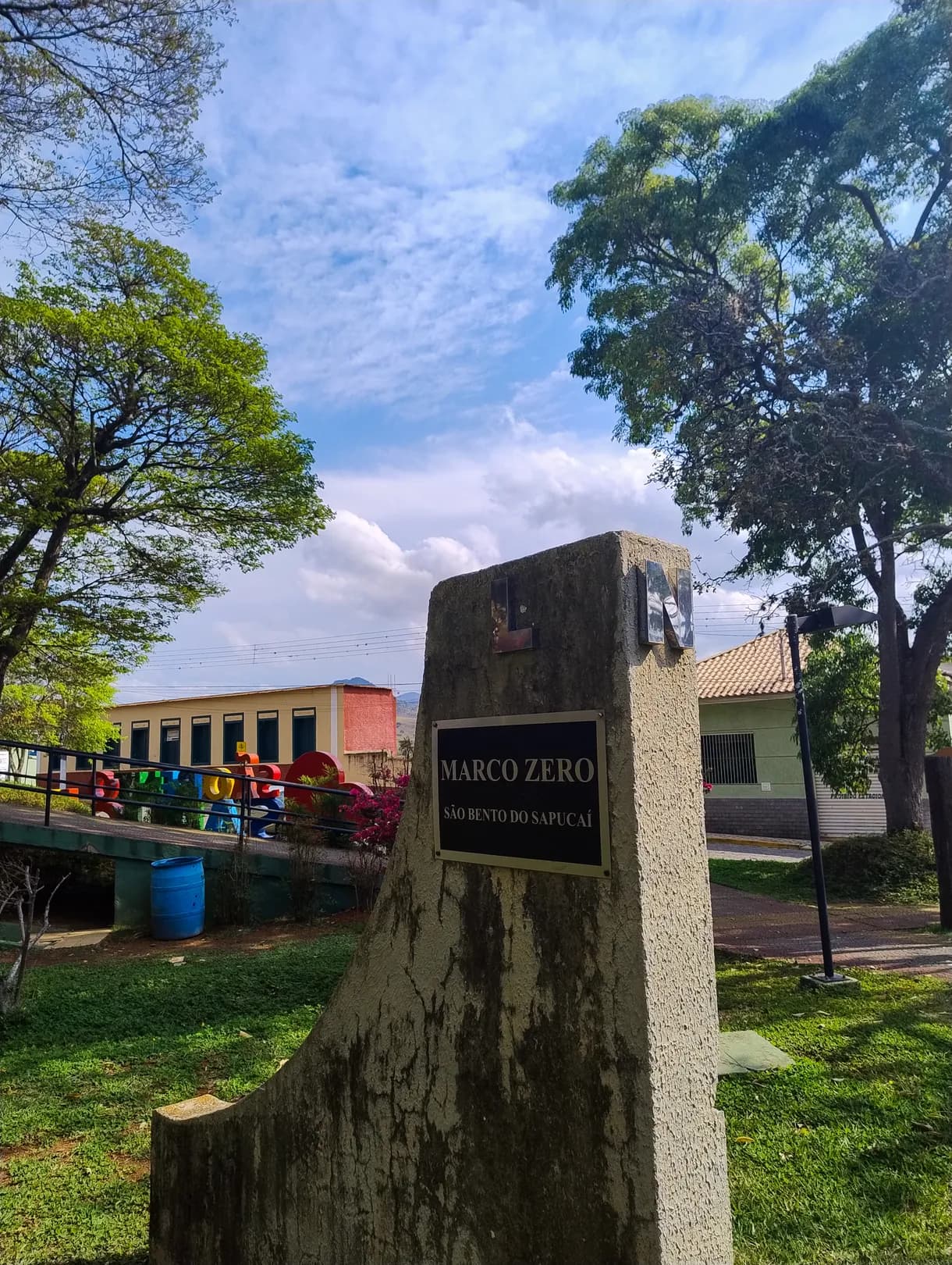 Marco zero de São Bento do Sapucaí: bloco de pedra com placa, no gramado arborizado da praça
