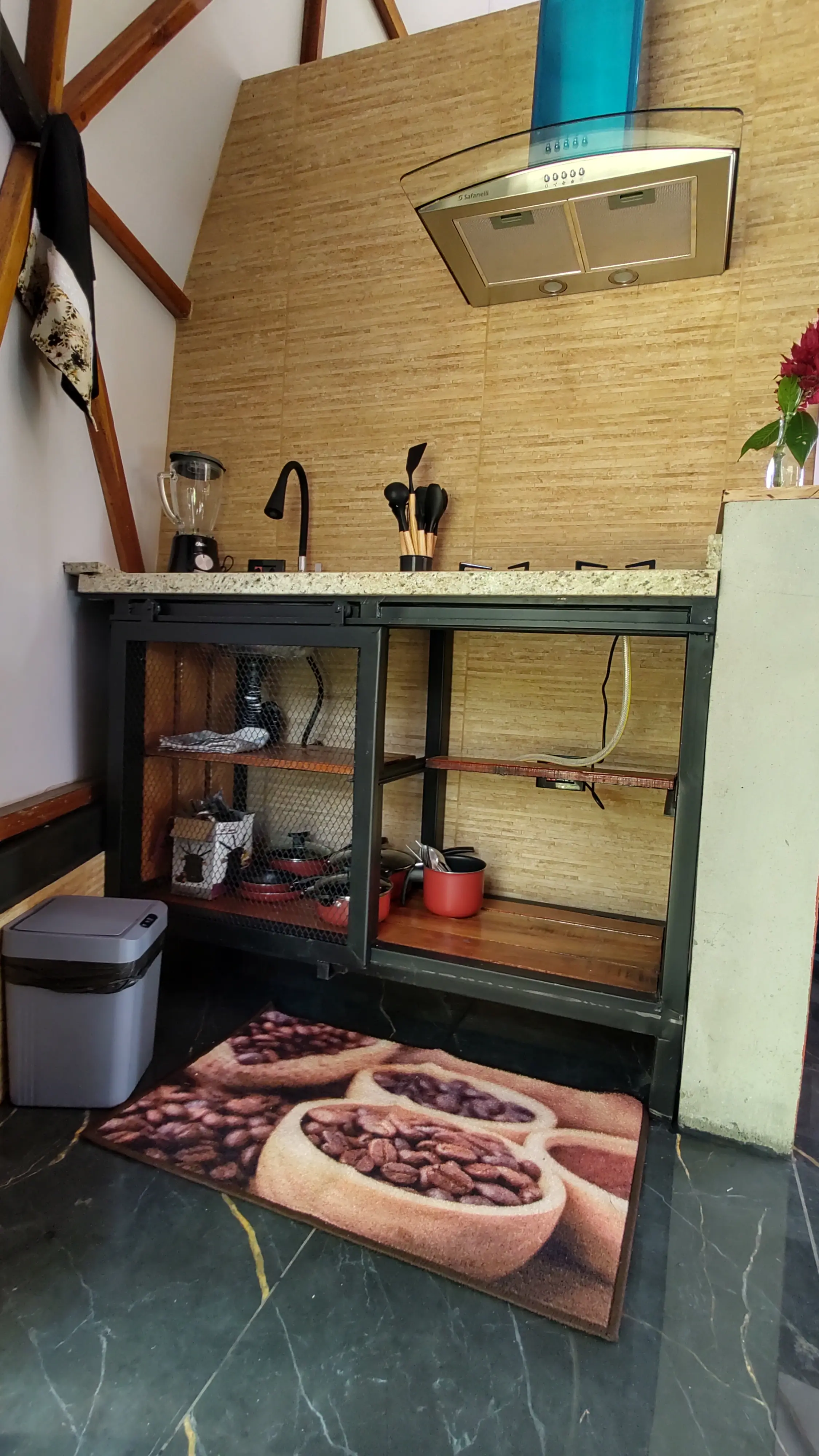 Bancada de granito com coifa, liquidificador e armário de utensílios, sob a estrutura inclinada do domo
