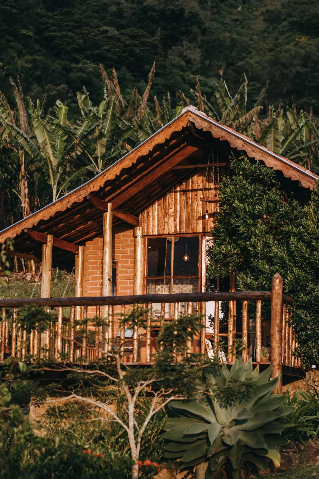 Fachada do Chalé Jade ao entardecer, com varanda de troncos, telhado de madeira e bananal ao fundo