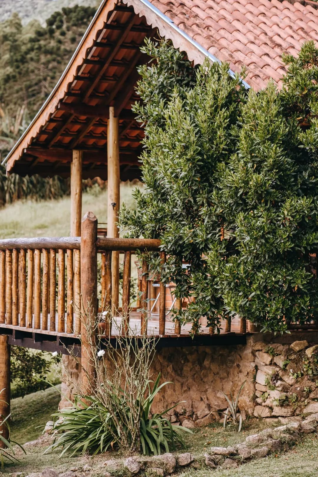 Deck de troncos do Chalé Jade sob o telhado de telha, apoiado em muro de pedra